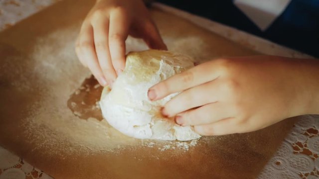 Close-up view of baby hand kneading dough on the table.