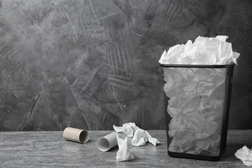Trash bin with used toilet paper on floor near grey wall. Space for text