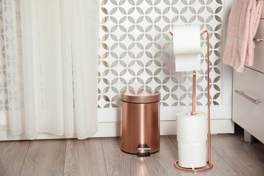 Toilet paper holder with rolls and trash bin in bathroom interior