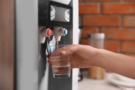 Woman filling glass with water from cooler indoors, closeup