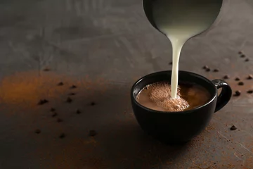 Poster Pouring milk into cup with tasty hot chocolate on table. Space for text © New Africa
