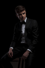 seated stylish man in black tuxedo looks to side