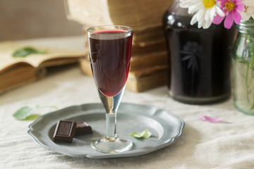 Cream de Cassis homemade blackcurrant liqueur in small glasses, books and flowers. Rustic style.