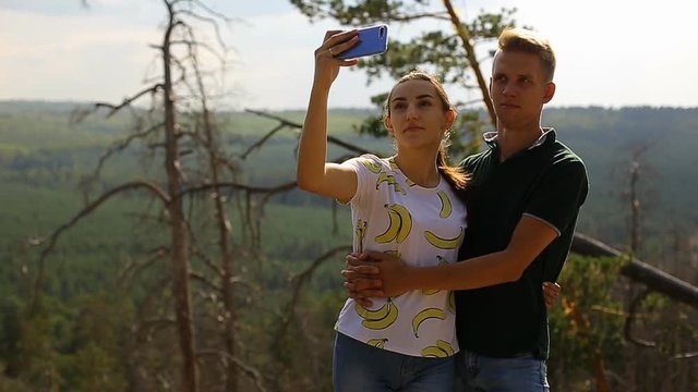 a guy and a girl doing a selfie on a smartphone in a pine forest on a bright Sunny day standing on a rock