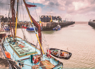 Fishing boats and huts in Whitstable harbour, Kent, UK. A small wooden rowing  boat can be seen...