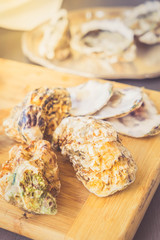 Raw oysters closed shells on wooden board, toned