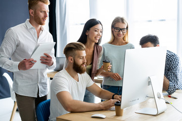 Discussing successful project. Group of young cheerful business people working and communicating while sitting at the office desk together with colleagues sitting in the background.