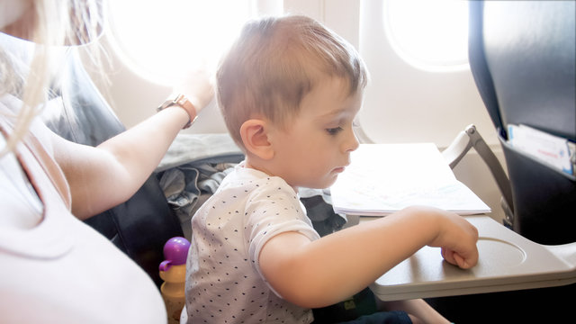 2 years old toddler boy flying with beautiful young mother in airplane