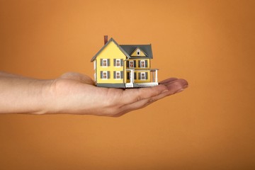 Fototapeta na wymiar Men's Hand Holding a Model of a House on Orange Background