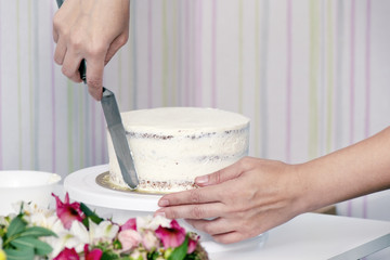 The confectioner's hands decorate the cake with white cream