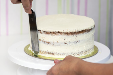 The confectioner's hands decorate the cake with white cream
