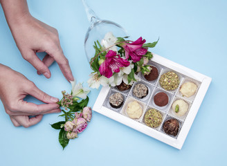the hands of the florist decorate with flowers a box of chocolates handmade from white chocolate and pistachios