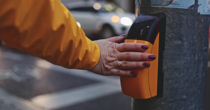 Woman Touching Traffic Light Regulation Sensor on a Pedestrian Crossing. SLOW MOTION 4K. Unrecogbizable Girl crosses the street in the city. Dusk Traffic on background. 