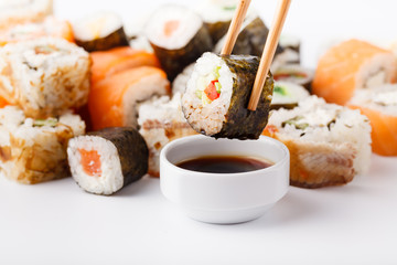 Two chopsticks holding Hosomaki roll with vegetables and different sushi rolls with seafood