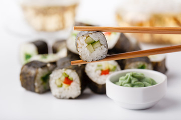 Two chopsticks holding Hosomaki roll with vegetables and different sushi rolls with seafood