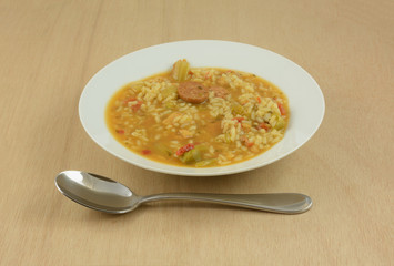 Chicken sausage gumbo soup with rice and vegetables in white soup bowl with large soup spoon on wooden table