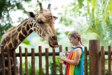 Naklejka premium Dzieci karmią żyrafę w zoo. Dzieci w parku safari.