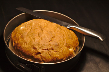 Freshly baked homemade bread in a round baking dish on a dark background
