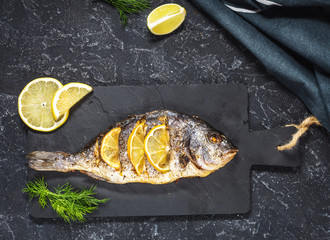Grilled fish on stone plate with lemon on dark background