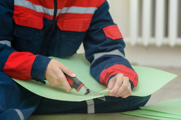 a young woman in workwear cuts a green laminate backing with a sharp blade. Insulated underlay on...