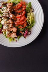 Meat salad with tomato served in white plate on dark table. Copy space