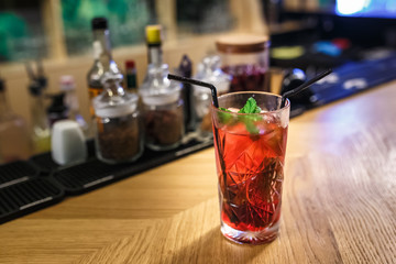 red cocktail in a glass with mint and two tubes on a table in a luxury bar