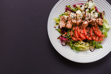Meat salad with tomato served in white plate on dark table. Copy space