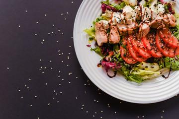 Meat salad with tomato served in white plate on dark table. Copy space