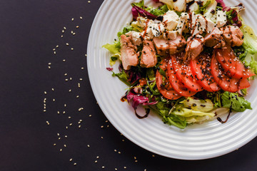 Meat salad with tomato served in white plate on dark table. Copy space