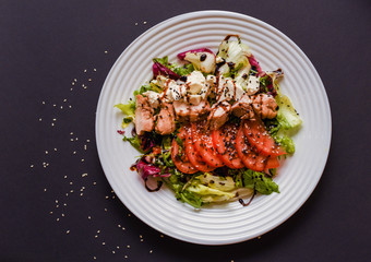 Meat salad with tomato served in white plate on dark table. Copy space