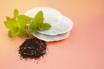 Paper round tea bags and mint leaves on pink background with copy space. Drinks and beverage.