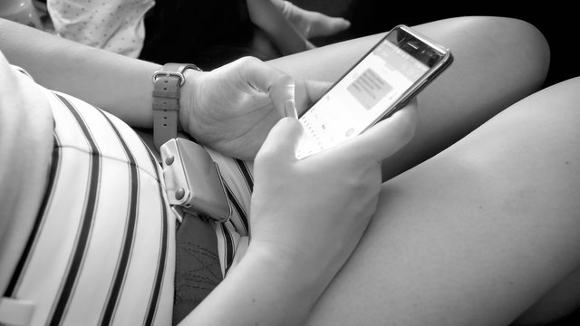 Black and white image of female airplane passenger typing sms on smartphone during flight