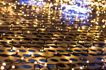 Fototapeta premium Christmas lights of garland on a metal grill with circles, cream color, background.