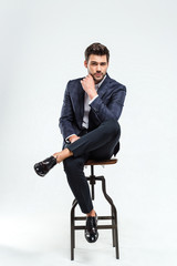  Elegant and handsome. Full length of handsome young man looking at camera while sitting against...