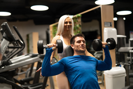 Woman helping man to do exercise with dumbbells
