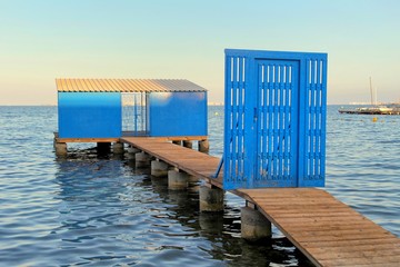 Lovely warm evening image of a blue gate barring the way to a private jetty or mooring, in a calm peaceful sea
