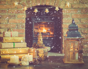 Obraz premium Christmas composition, lantern, presents and decorations on the table in front of fireplace with woodburner, Christmas tree with baubles and ornaments and garlands, snow, selective focus, toned