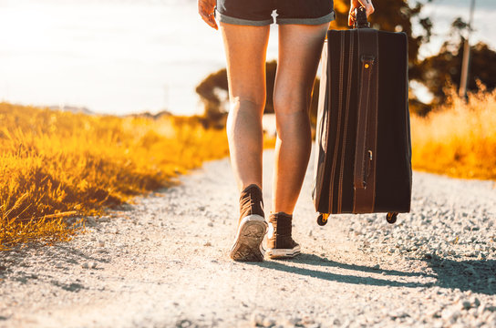Close up of legs of a woman at vacation walking on the road holding her suitcase on a countryside background