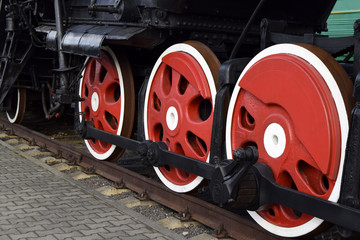 Fragment of the ancient locomotive. Red wheels of the black locomotive are on rails. Close up.