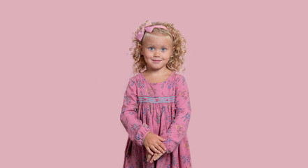 Cute 3-year old blond girl in a pink outfit with beautiful green eyes. Pink background