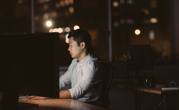 Young Asian businessman sitting at his workstation late at night