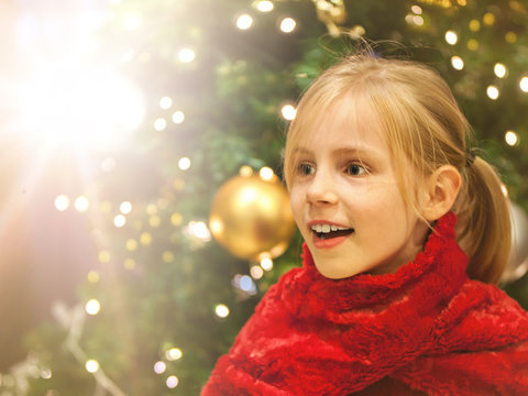 M&auml;dchen sieht &uuml;berrascht sein Geschenk zu Weihnachten und steht vor dem geschm&uuml;ckten Weihnachtsbaum