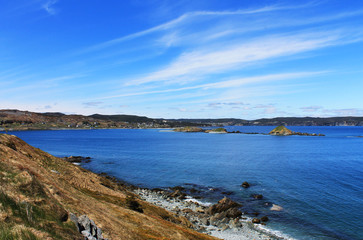 Naklejka premium Looking along the cliffs and the coastline at the Atlantic Ocean, and the community of Ferryland, Newfoundland. Lots of blue sea, and blue sky with light, wispy clouds. 