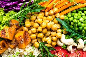 Bowl dish with brown rice, cucumber, tomato, green peas, red cabbage, chickpea, fresh lettuce salad and cashew nuts. Healthy balanced eating