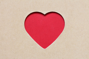 A red heart is visible through a heart-shaped cutout in kraft paper. Concept of: Simple affection