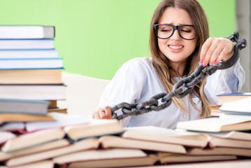 Young female student chained to the desk and preparing for exams