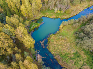 Aerial top view of autumn forest and blue river with small whirlpool.