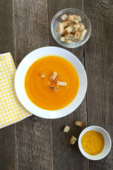 Pumpkin soup in a white plate with croutons and curry seasoning