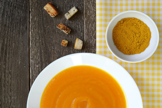Pumpkin soup in a white plate with croutons and curry seasoning