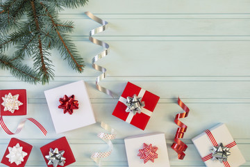 On a light blue background lie holiday gifts with bows. There is a branch of a Christmas tree and a lot of beautiful ribbons.